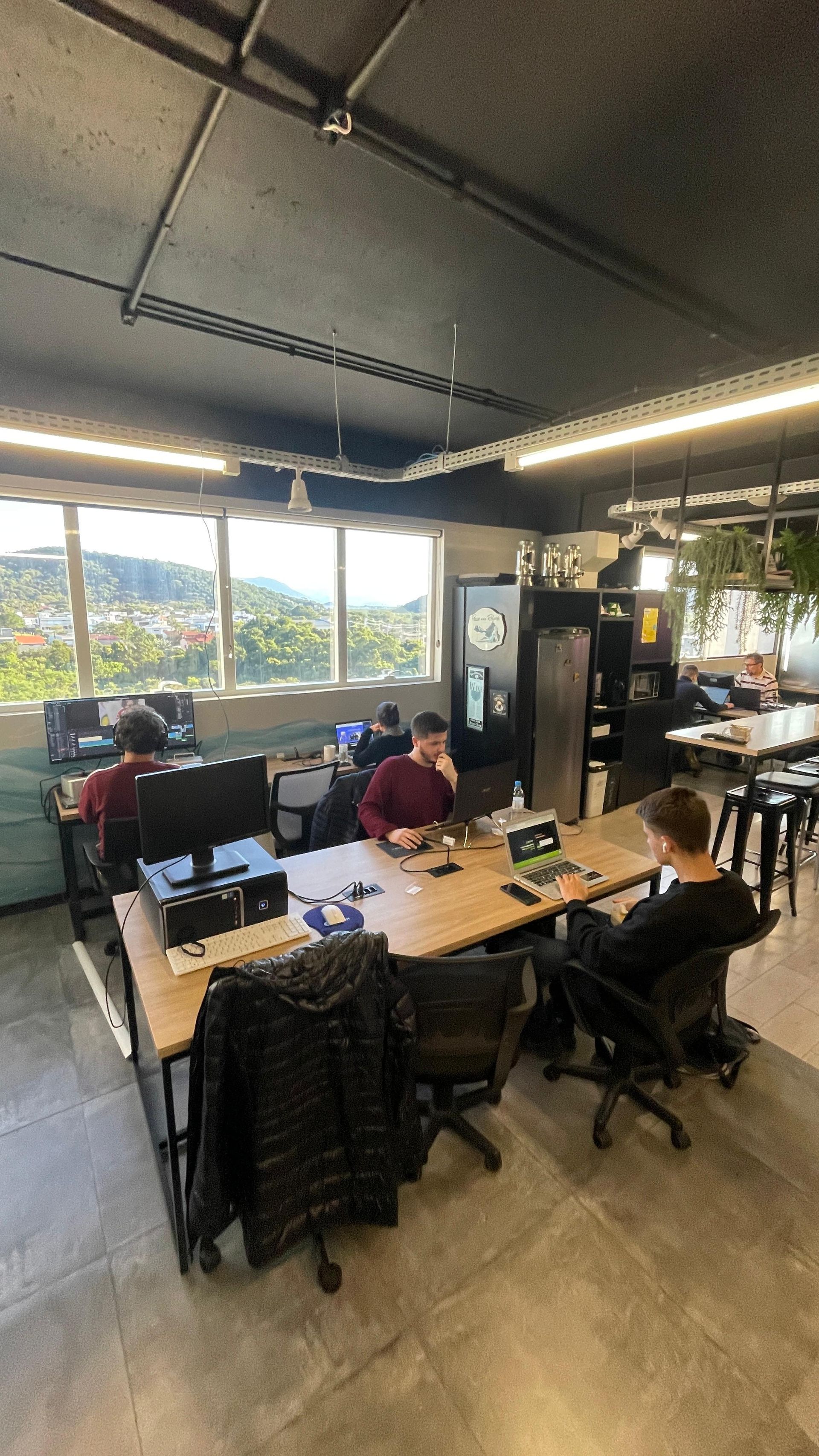 Um grupo de pessoas está sentado em mesas em um escritório no Sandbox Coworking