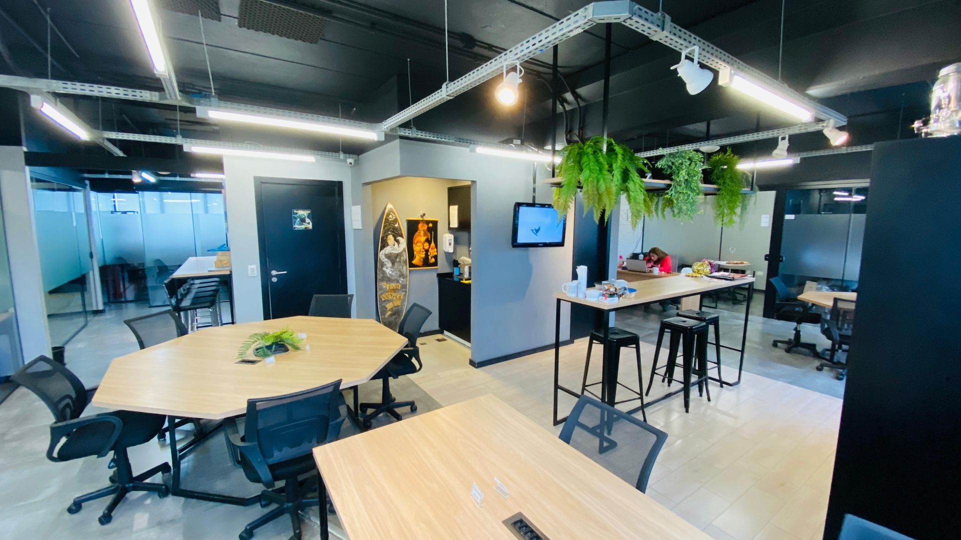 Sala de estar moderna com mesas redondas, cadeiras pretas, plantas suspensas e um biombo fixado na parede.