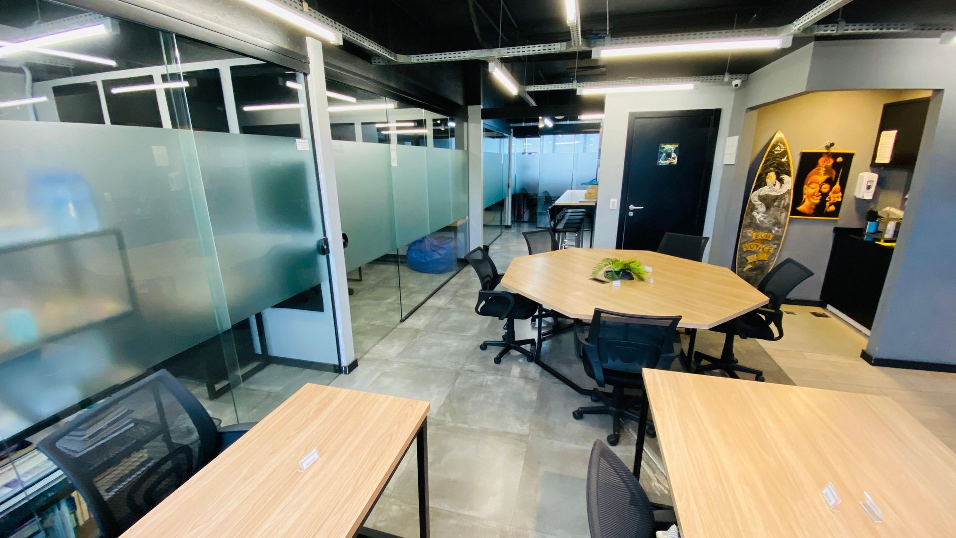 Sala de reuniões moderna com mesas redondas, cadeiras pretas, paredes de vidro e iluminação suspensa.
