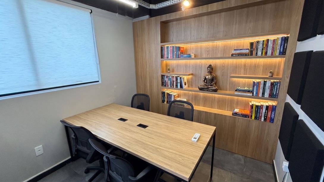 Escritório compartilhado com pessoas trabalhando em mesas, computadores e uma grande janela com vista para as colinas.
