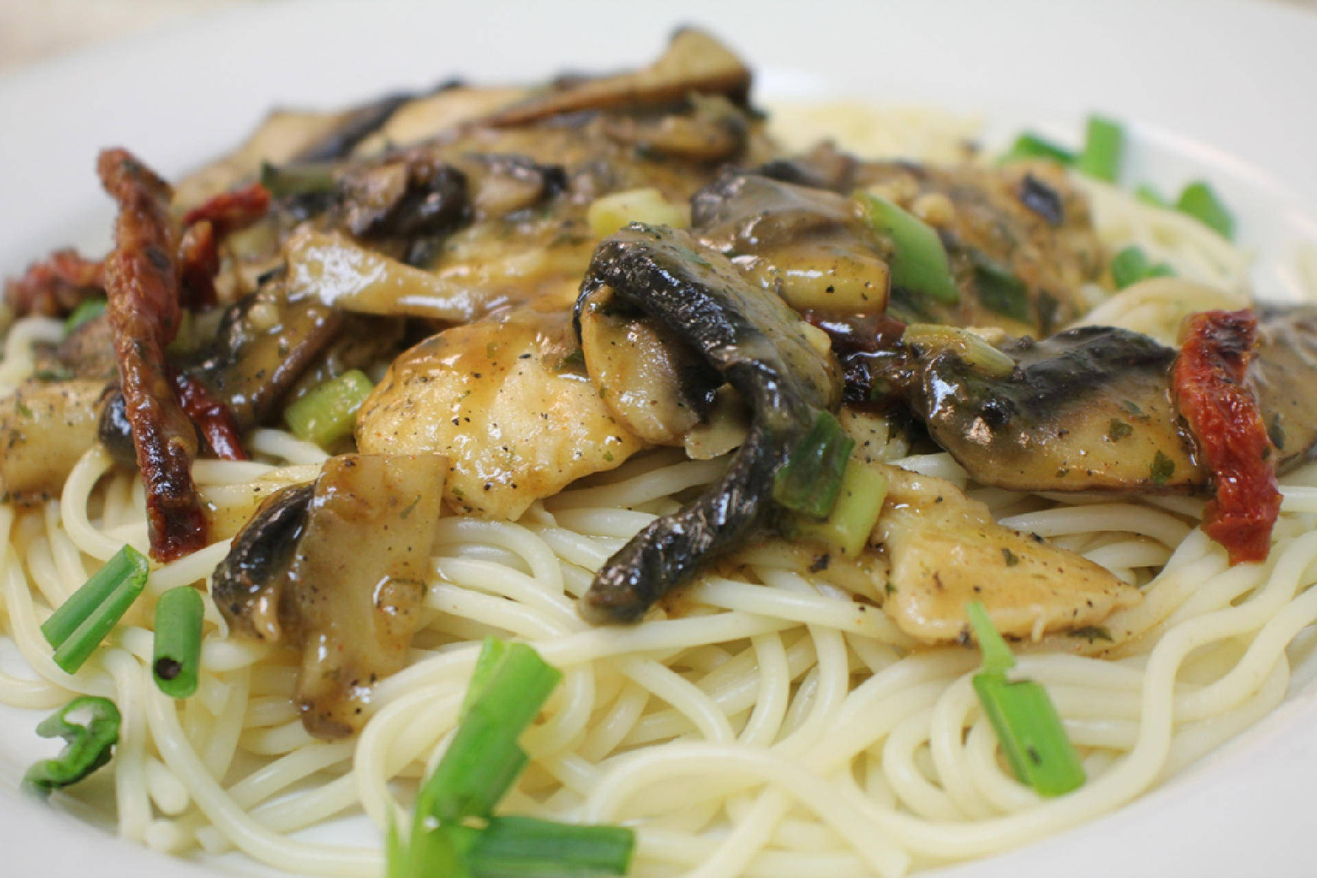 A succulent chicken breast in a rich sherry wine sauce, topped with sautéed portobello mushrooms, sun-dried tomatoes, and fresh chives, served over a bed of spaghetti pasta.