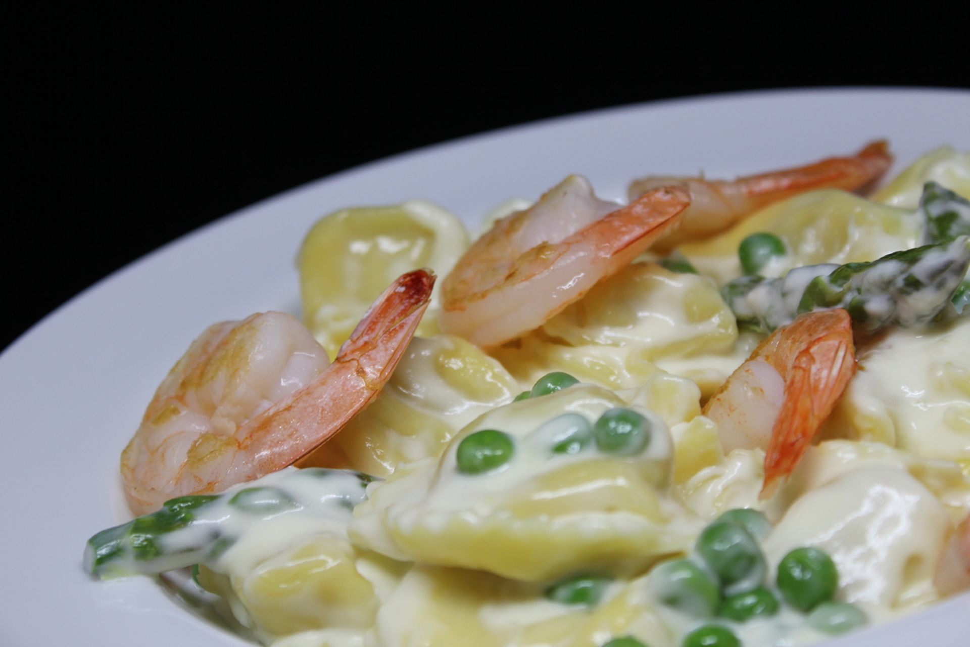 A mouth-watering dish of cheese tortellini pasta tossed in a zesty lemon cream sauce, complemented by succulent shrimp, tender asparagus, and sweet peas.