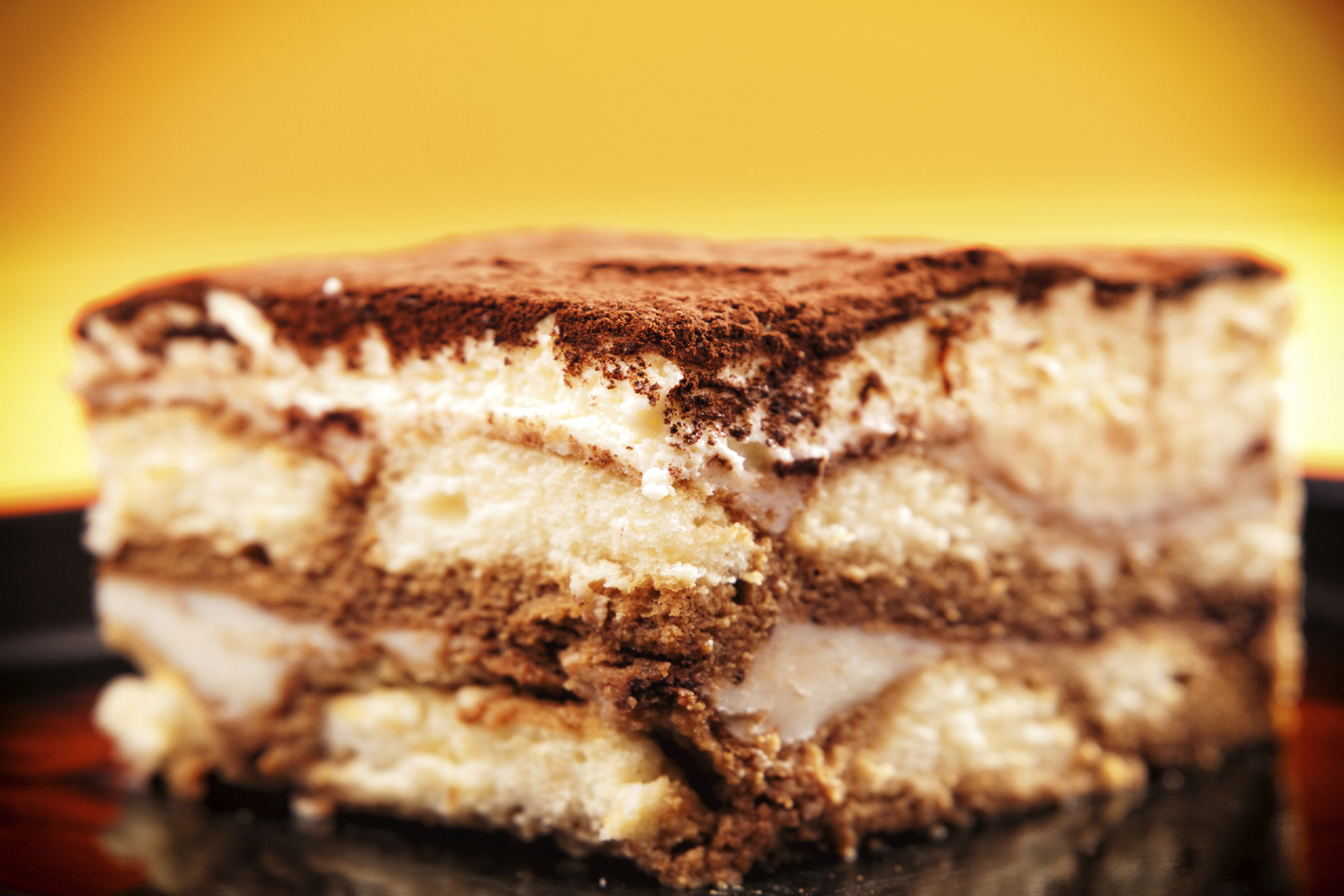 A delectable slice of tiramisu, featuring layers of espresso-soaked ladyfingers, creamy mascarpone cheese, and a dusting of cocoa powder.