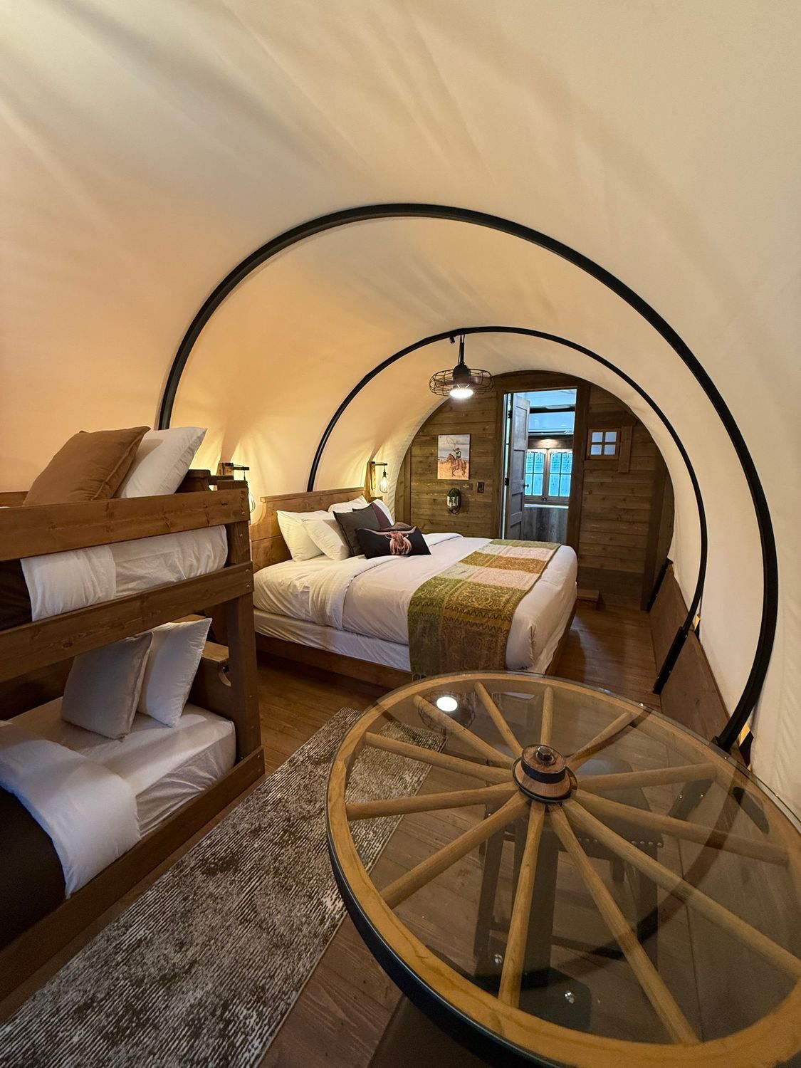 Cozy bedroom with twin beds, circular bed frames, warm lighting, and a wooden wagon-wheel table