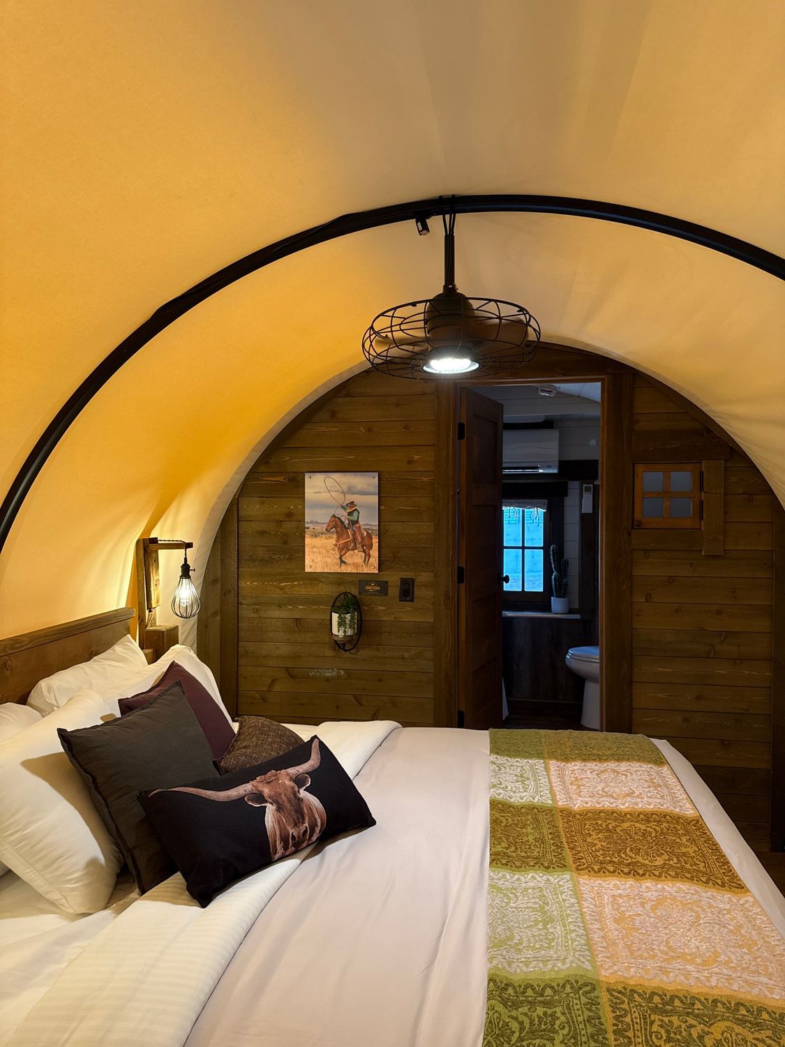 Cozy arched bedroom with a yellow ceiling, wooden door, and a bed with white and patterned bedding