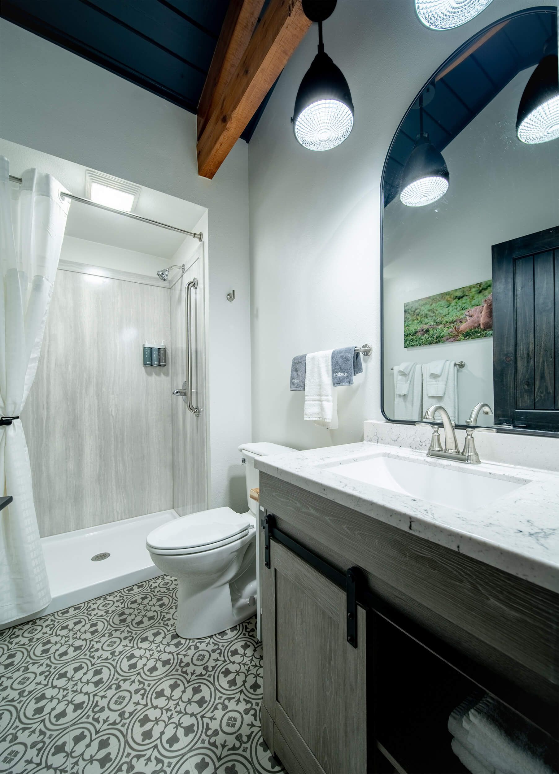 Modern bathroom with patterned tile floor, white vanity, toilet, shower, and pendant lights