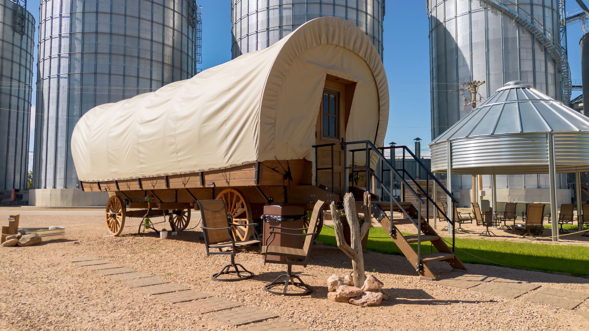Covered wagon on display in a plaza, with modern glass buildings in the background.