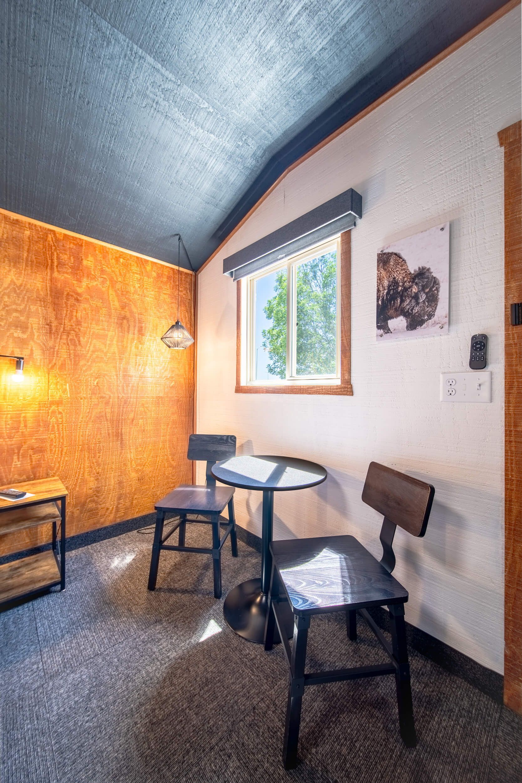 Small room with orange and white walls, two chairs, a round table, and a window under a blue ceiling.