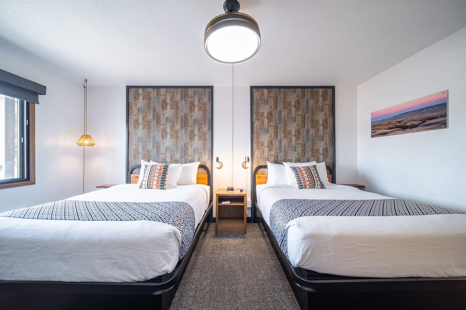 Two twin beds in a modern bedroom with gray walls, hanging lights, and framed artwork.