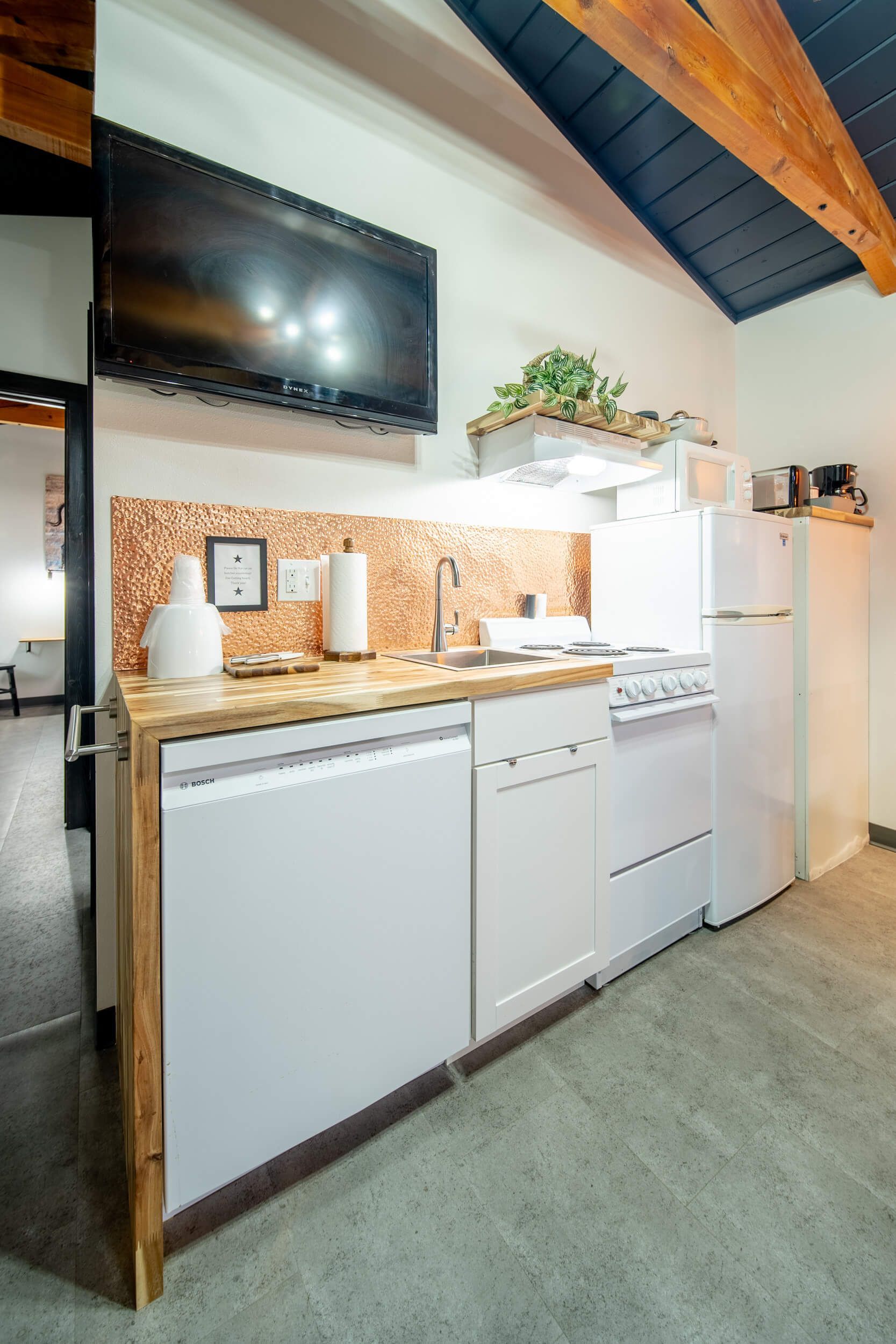 Small kitchen with white appliances, wood countertops, tiled backsplash, and a ceiling-mounted TV in a loft space