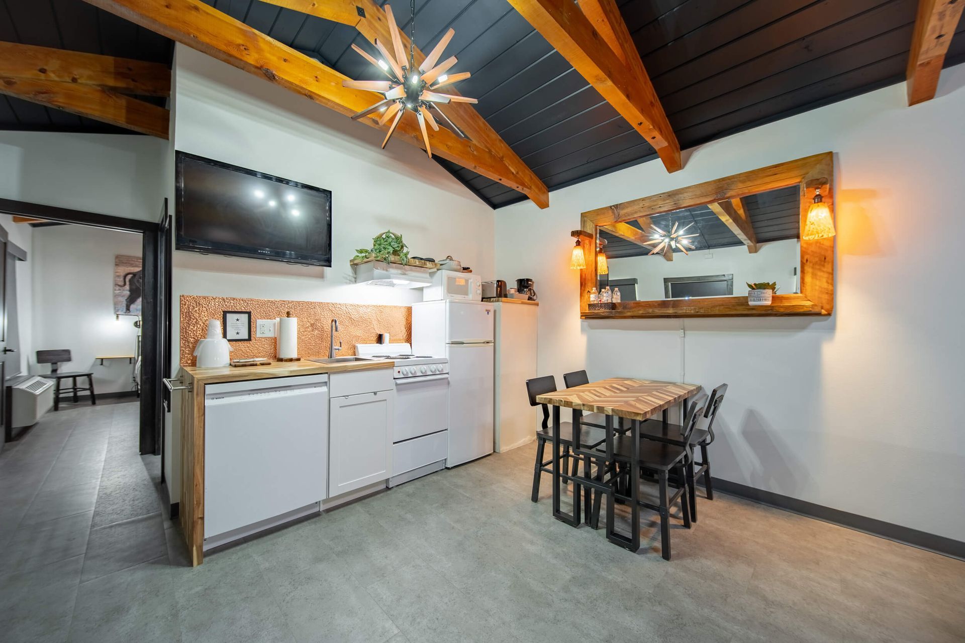 Cozy kitchen-dining area with white cabinets, wood ceiling, and small dining table near a mirror.