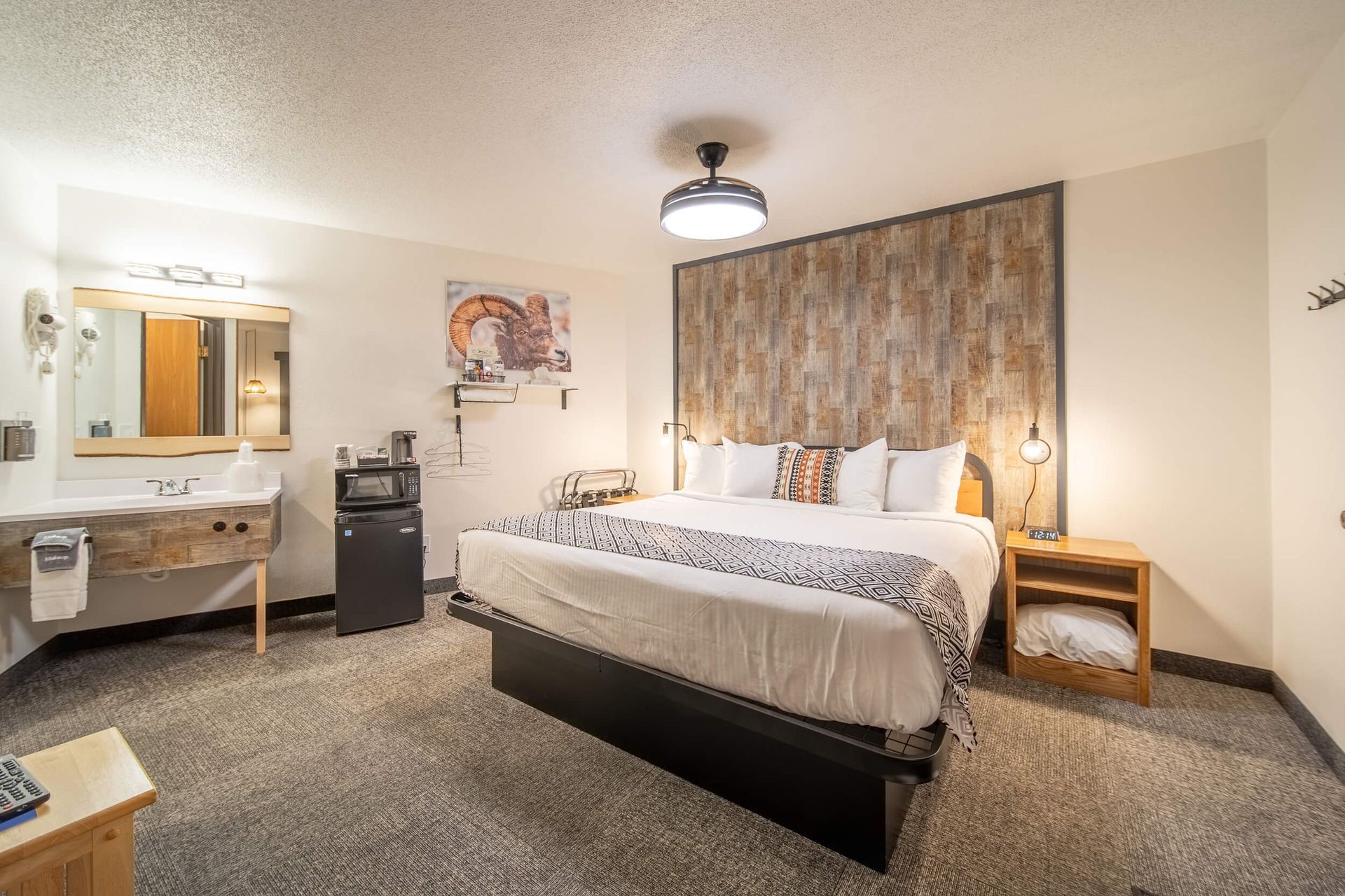 Hotel room with king bed, desk, nightstands, wall art, and carpeted floor