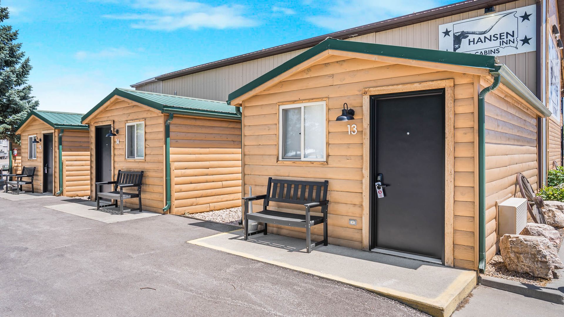 Row of small wooden cabin-style buildings with benches and a paved walkway under a clear sky