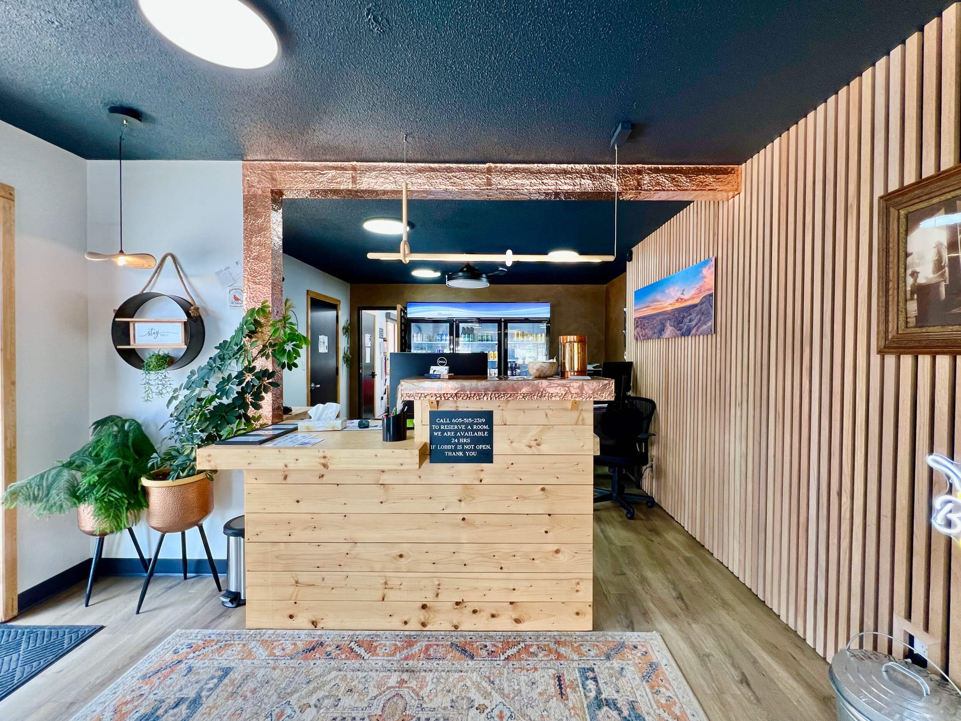 Modern lobby with wood reception desk, potted plants, and black ceiling in a stylish office interior