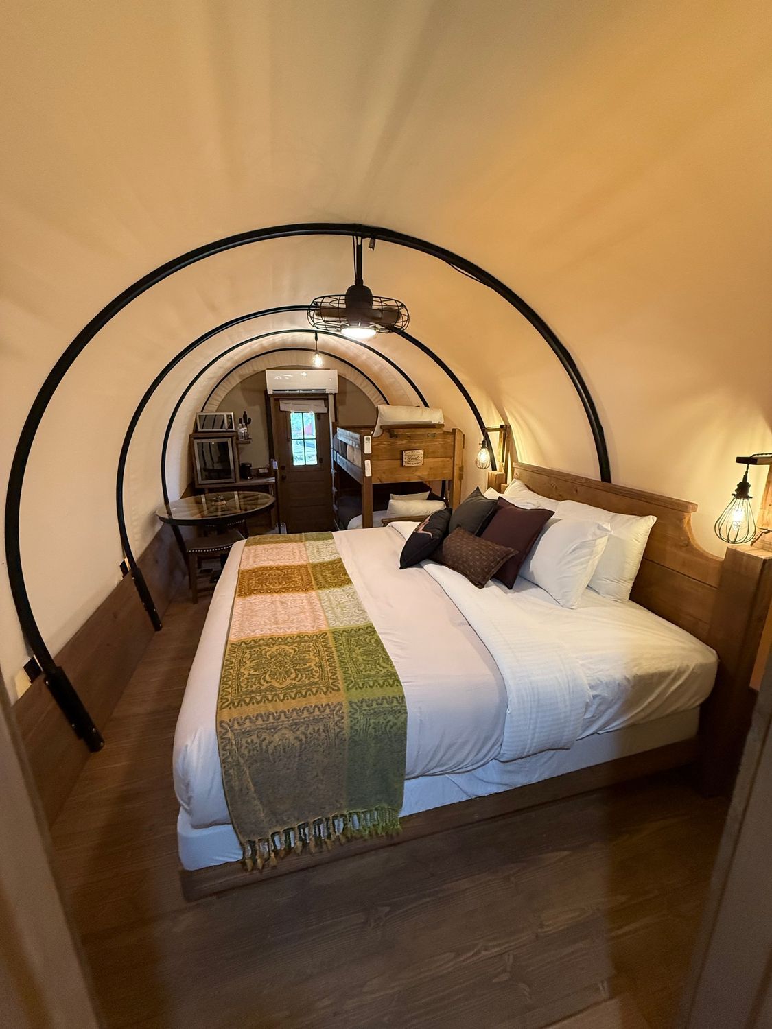 Cozy bedroom with arched wooden ceiling, white bed, colorful runner, and warm ambient lighting