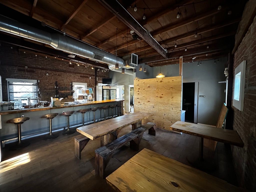 Rustic bar interior with wooden tables, long counter, and exposed beams under dim lighting