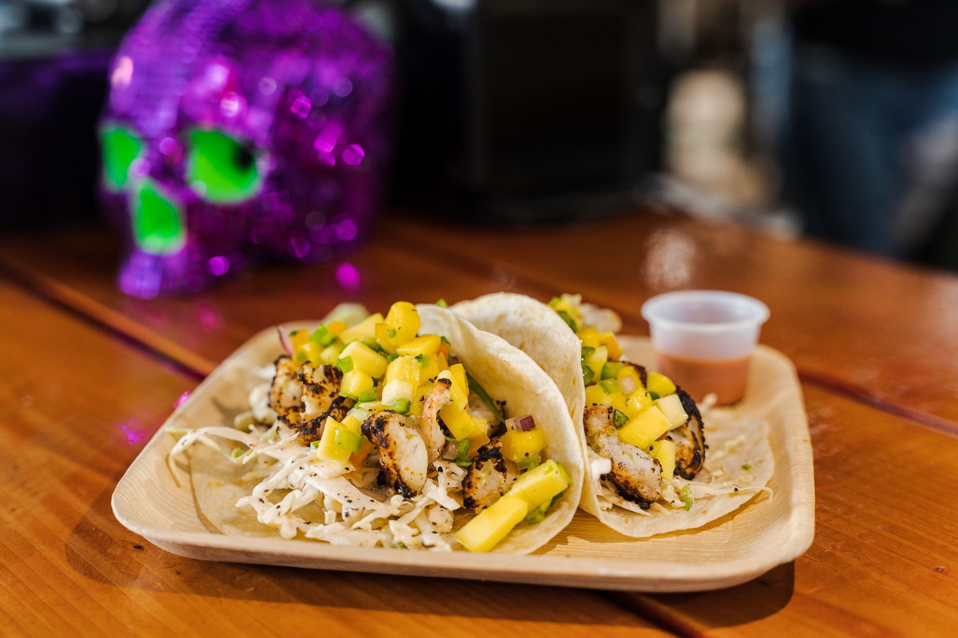 Two tacos on a tray with pineapple salsa and sauce cups on a wooden table