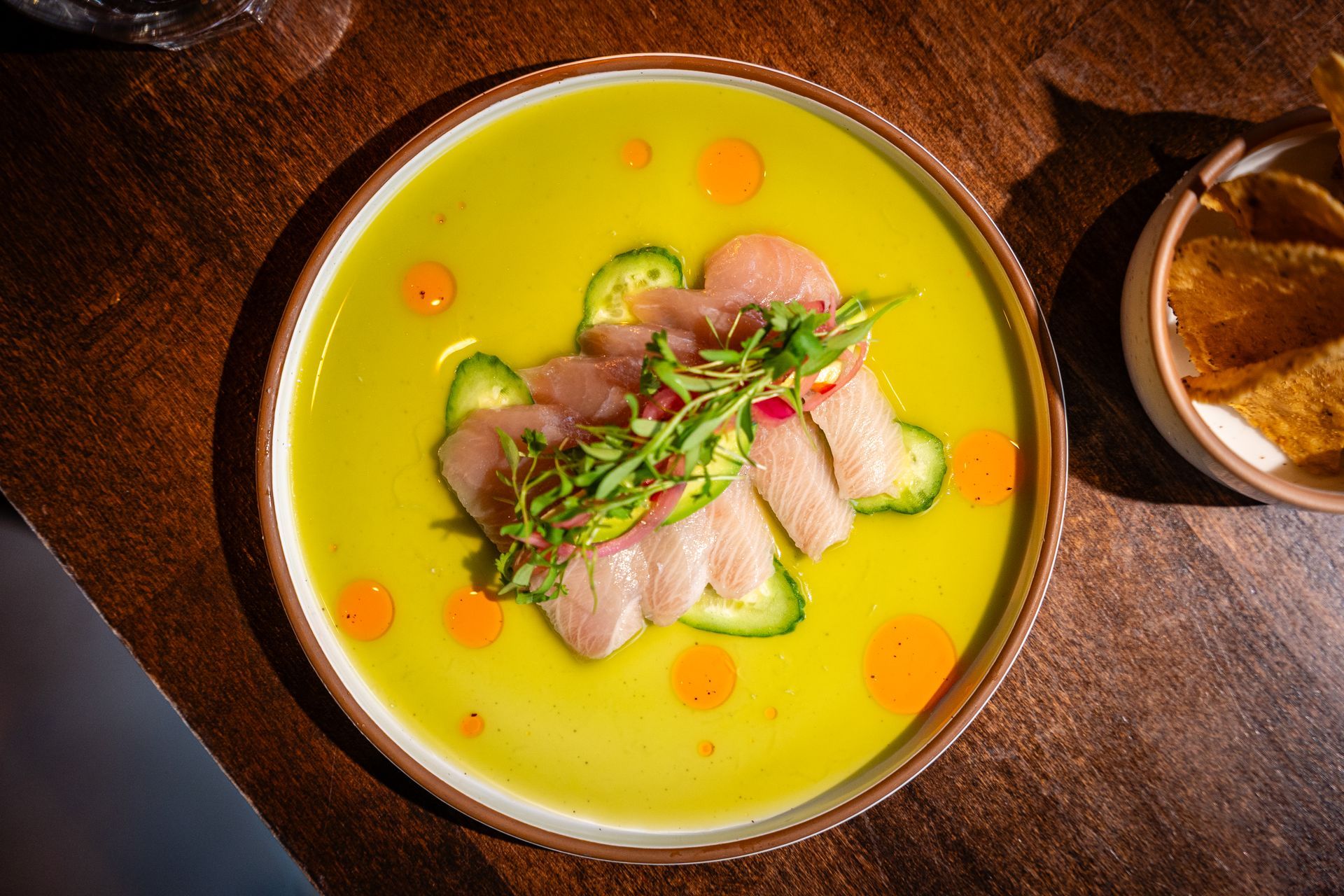 Bowl of green soup topped with sliced meat and herbs on a wooden table