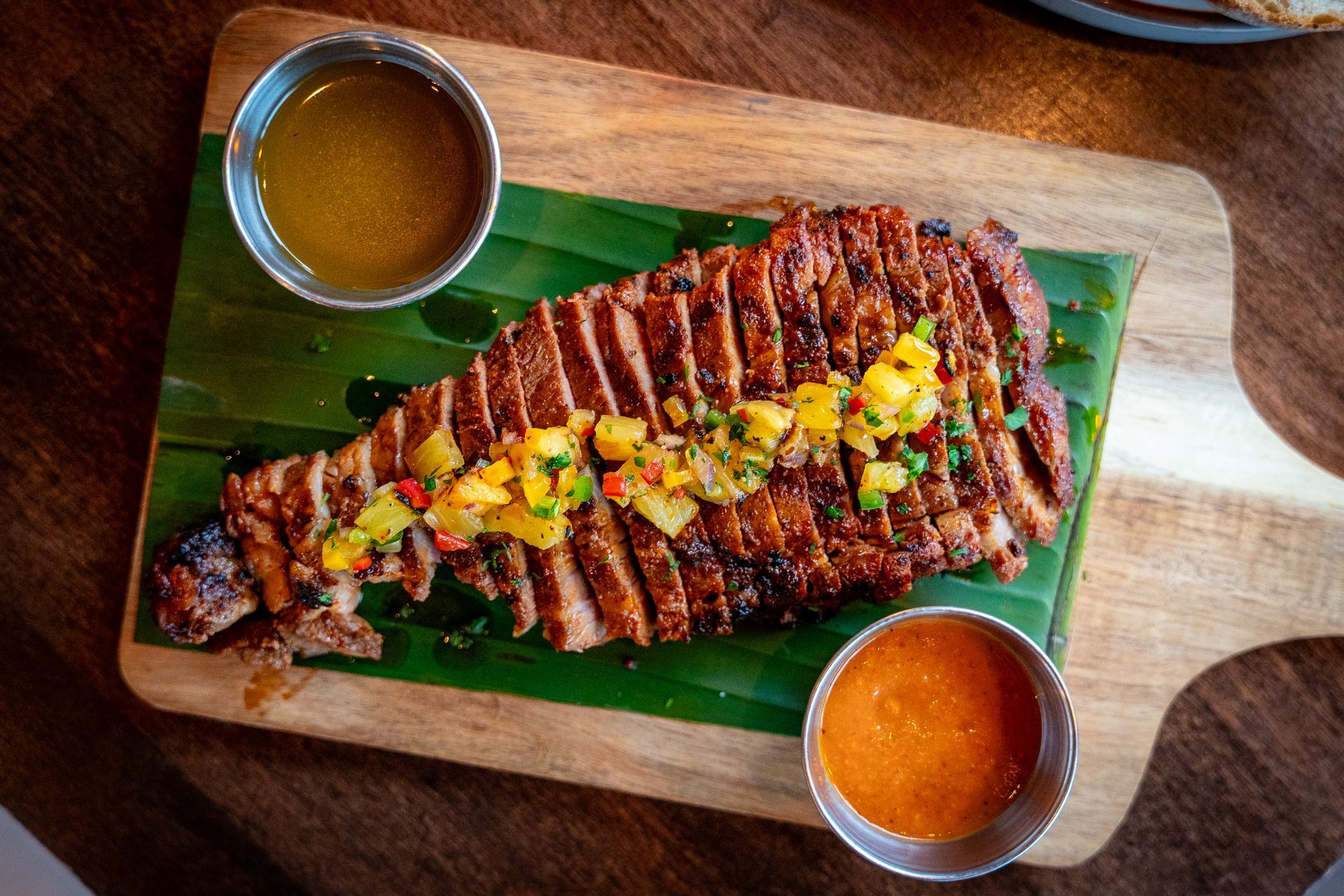 Grilled fish on a banana leaf platter with two dipping sauces and a corn garnish