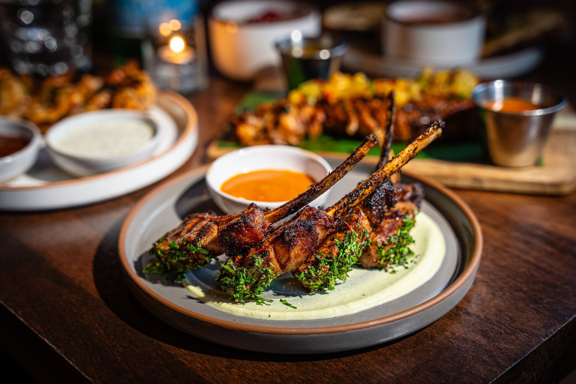 Grilled lamb chops on a plate with green sauce and orange dip on a restaurant table