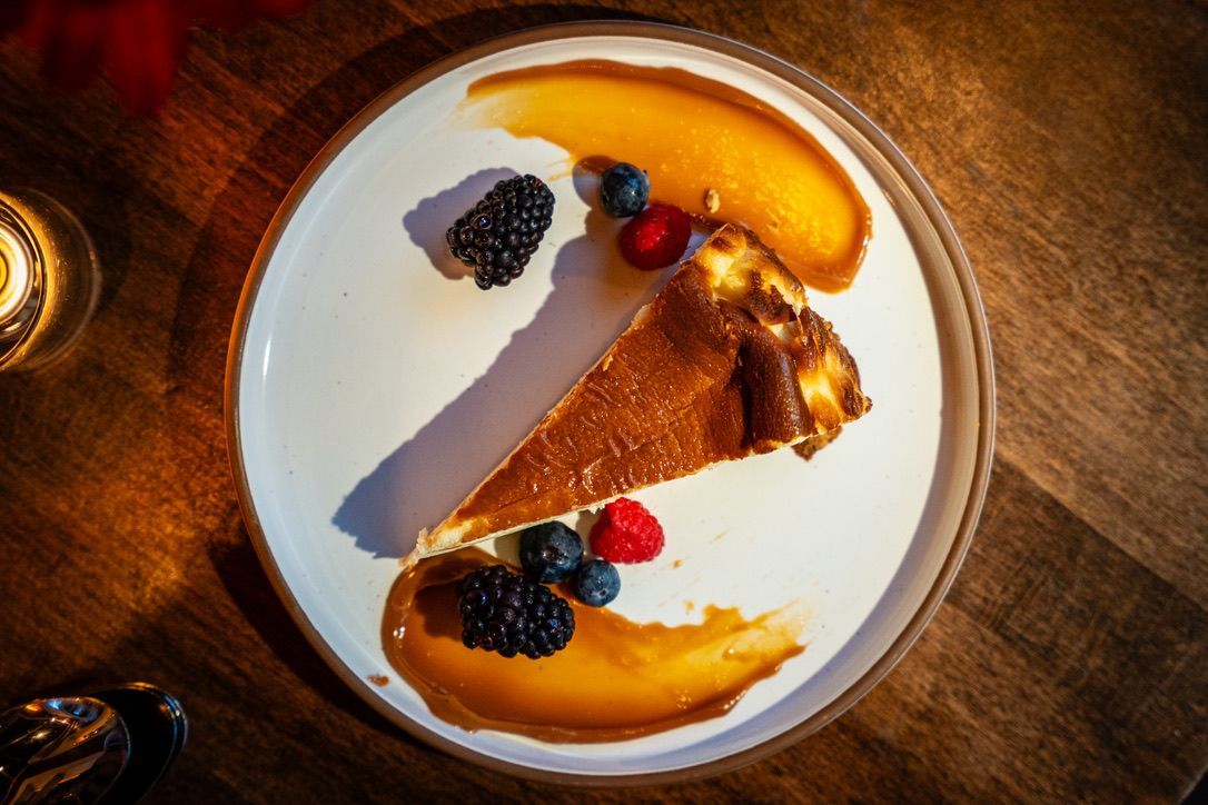 Slice of chocolate tart on a white plate with berries and orange sauce on a wooden table