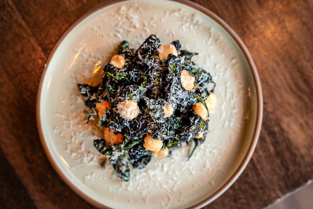 Bowl of creamy white soup topped with dark greens and toasted nuts on a wooden table