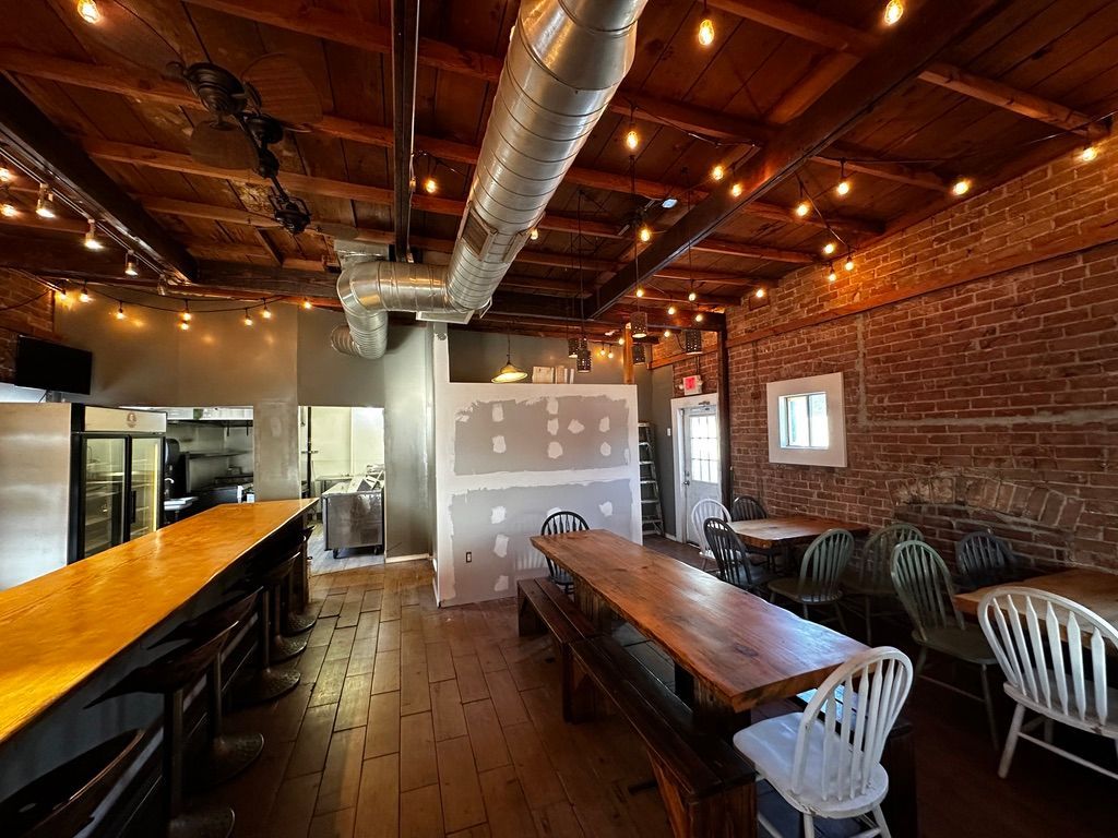 Empty industrial-style restaurant interior with long wooden tables, brick walls, and warm pendant lighting