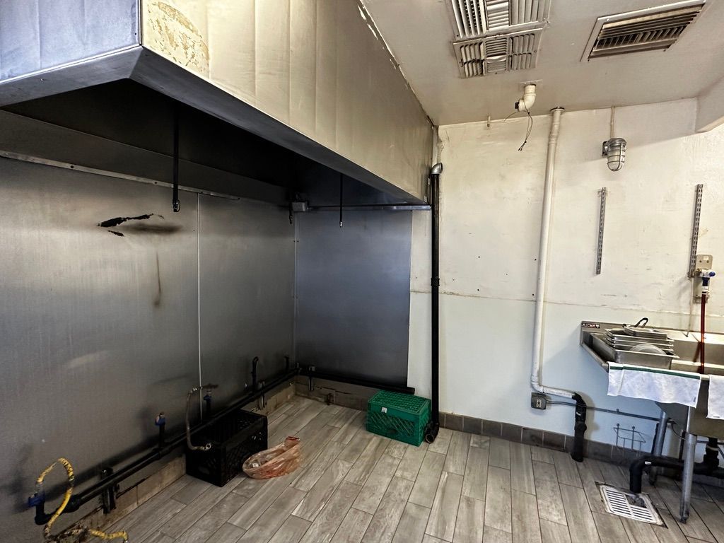 Empty commercial kitchen with stainless steel walls, hood vent, sink, and tiled floor