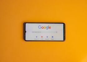A smartphone on an orange background displaying the Google homepage in landscape orientation
