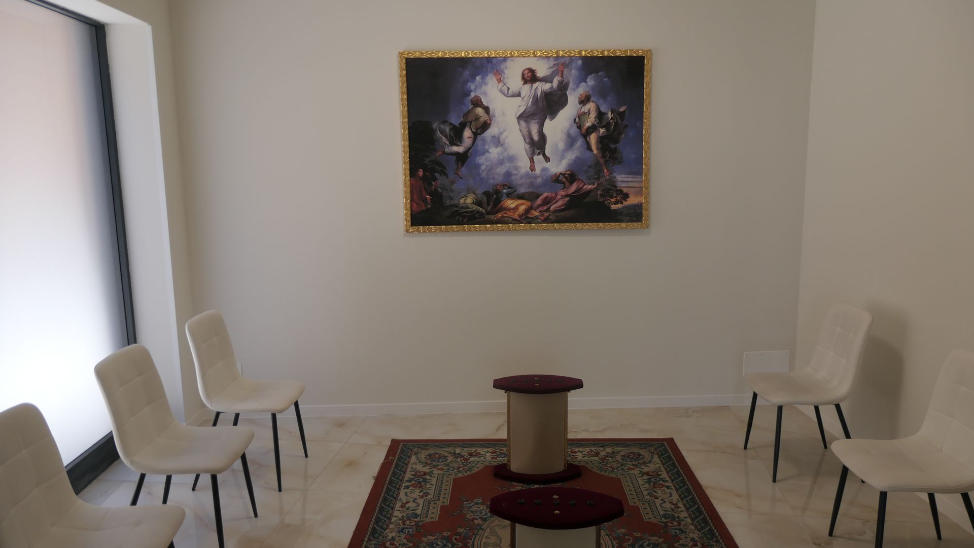 Stanza con sedie attorno a un piccolo altare su un tappeto decorato; un dipinto sul muro.