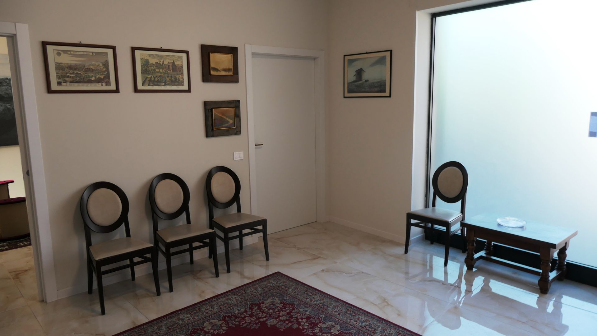 Una sala d'attesa con sedie, opere d'arte, un tappeto e una finestra in vetro smerigliato.