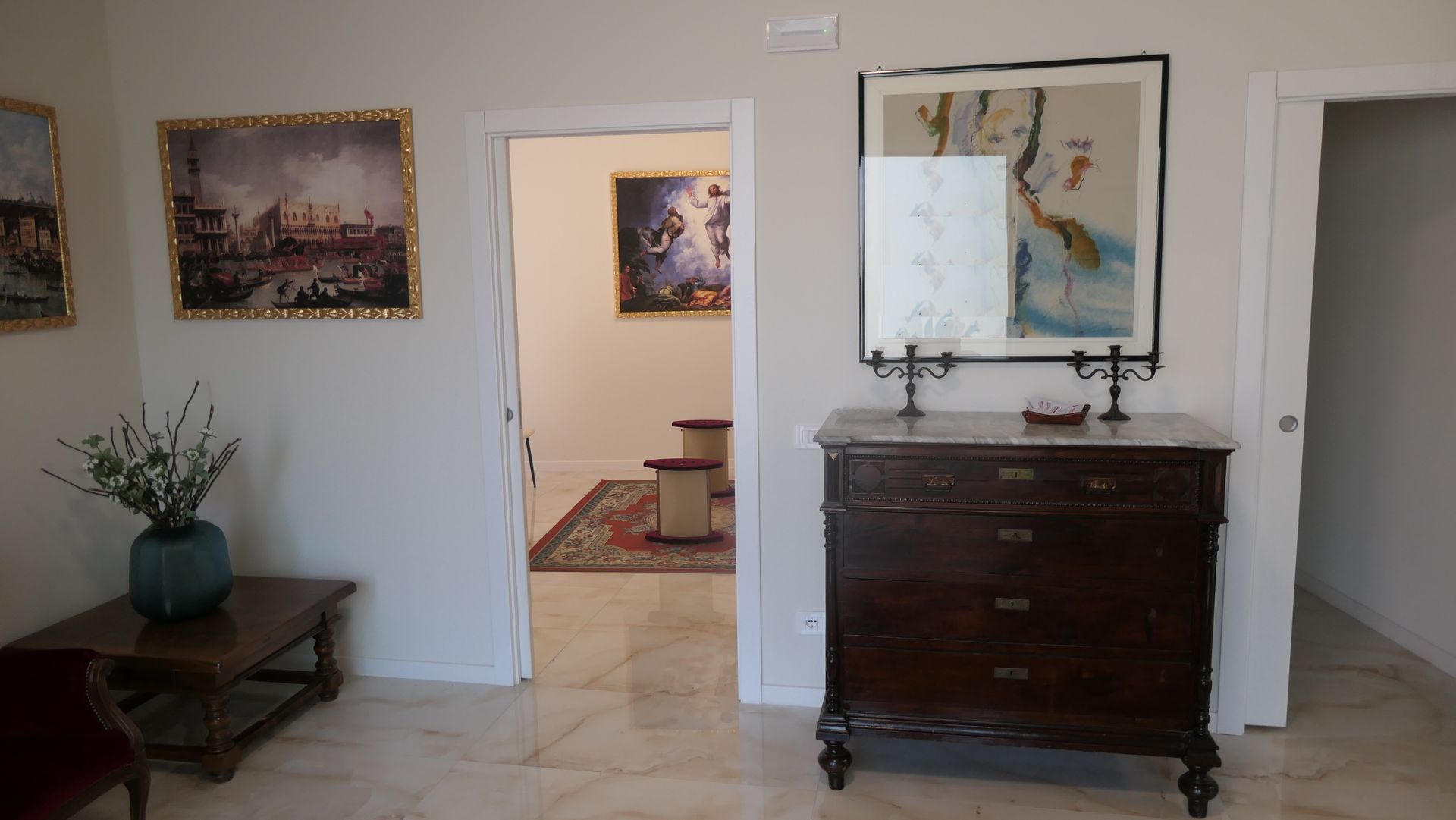 Corridoio con opere d'arte, baule in legno scuro e porte aperte verso altre stanze.