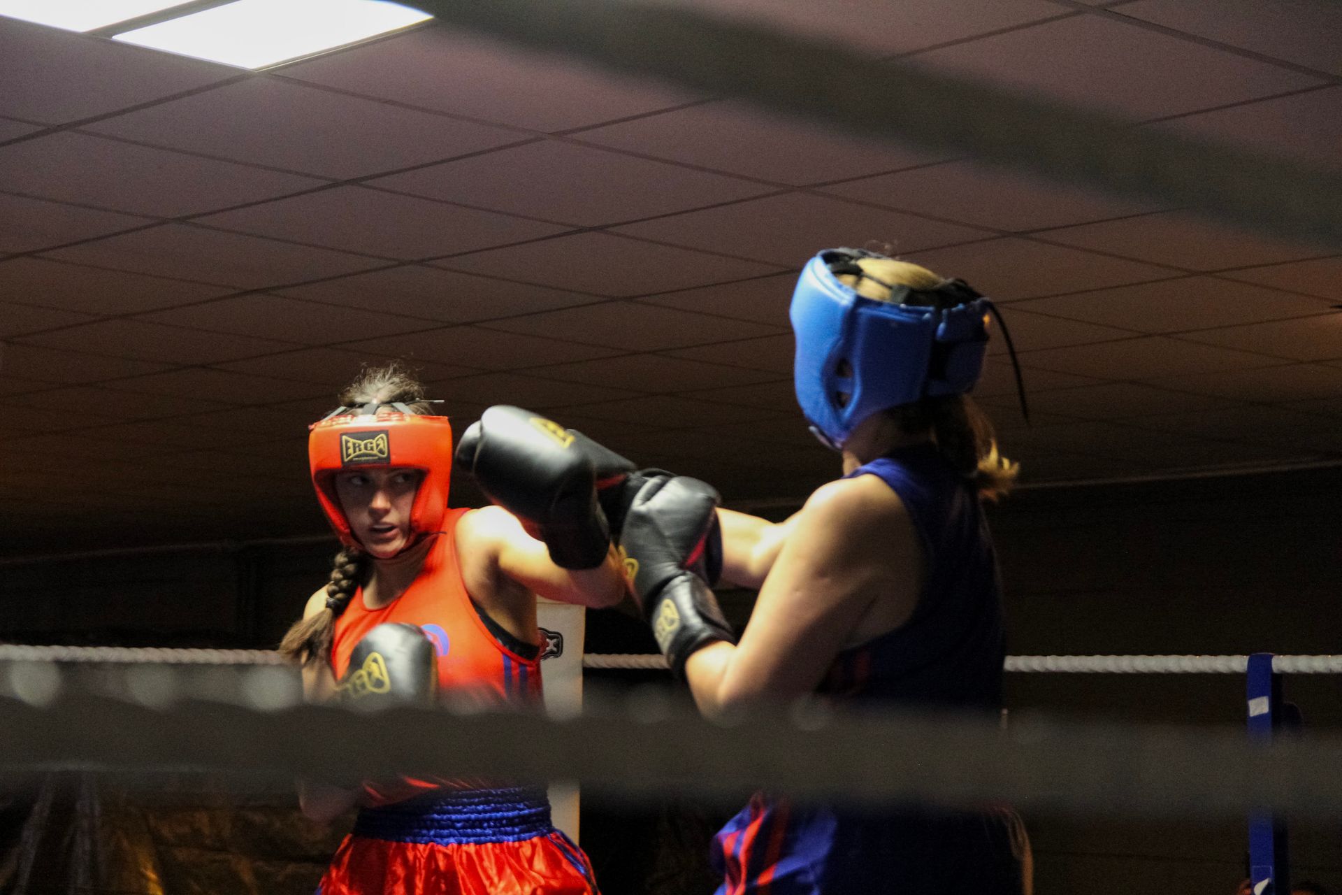 Two boxers in a ring; one throws a punch. Both wear headgear and gloves, red and blue outfits.