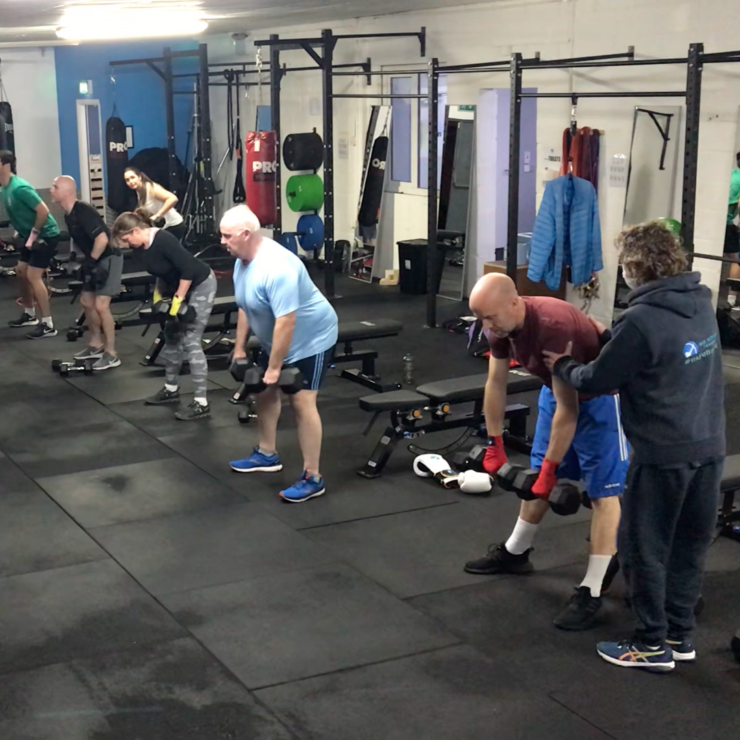 People working out with dumbbells in a gym, assisted by a coach.