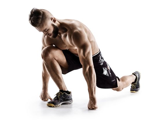 Man in workout gear performing a low lunge with arms extended for balance.