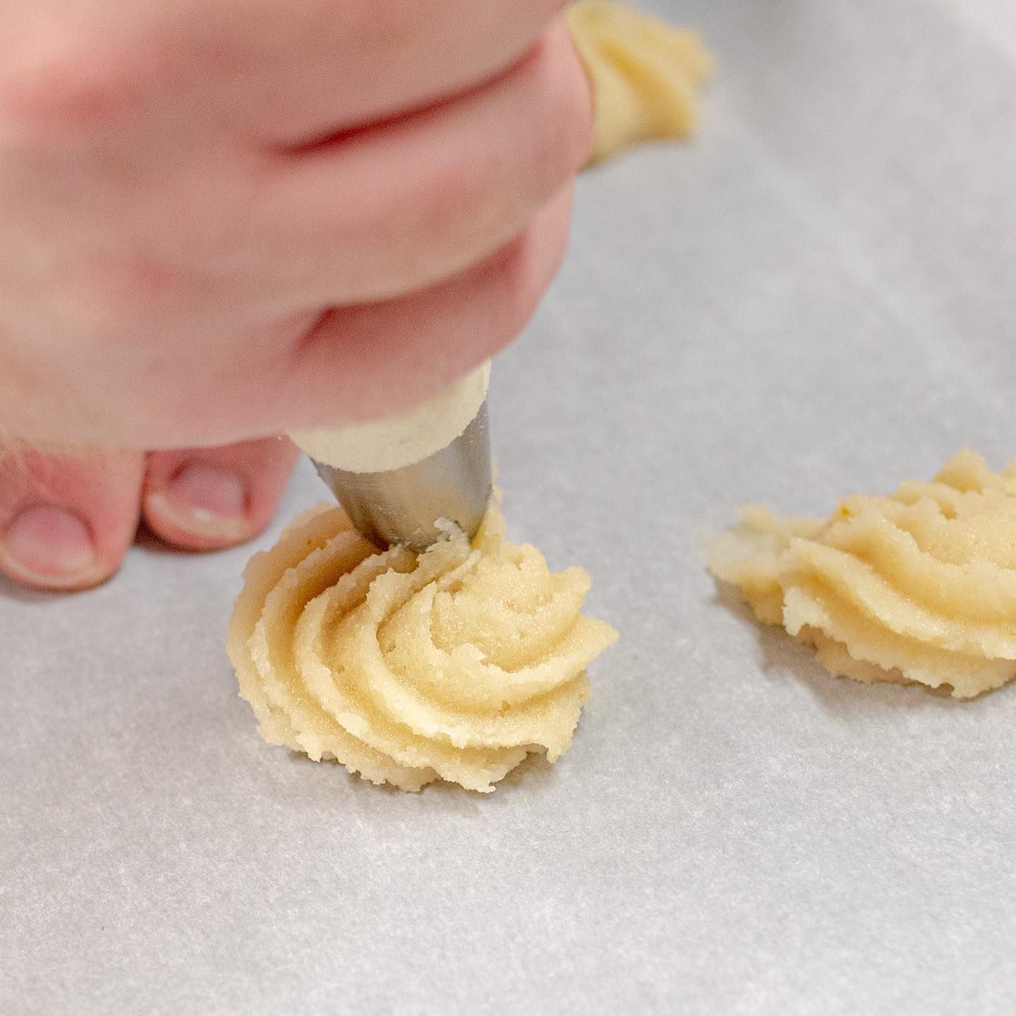Una persona usa una sac à poche con punta a stella per creare riccioli di pasta per biscotti su una teglia rivestita di carta da forno.