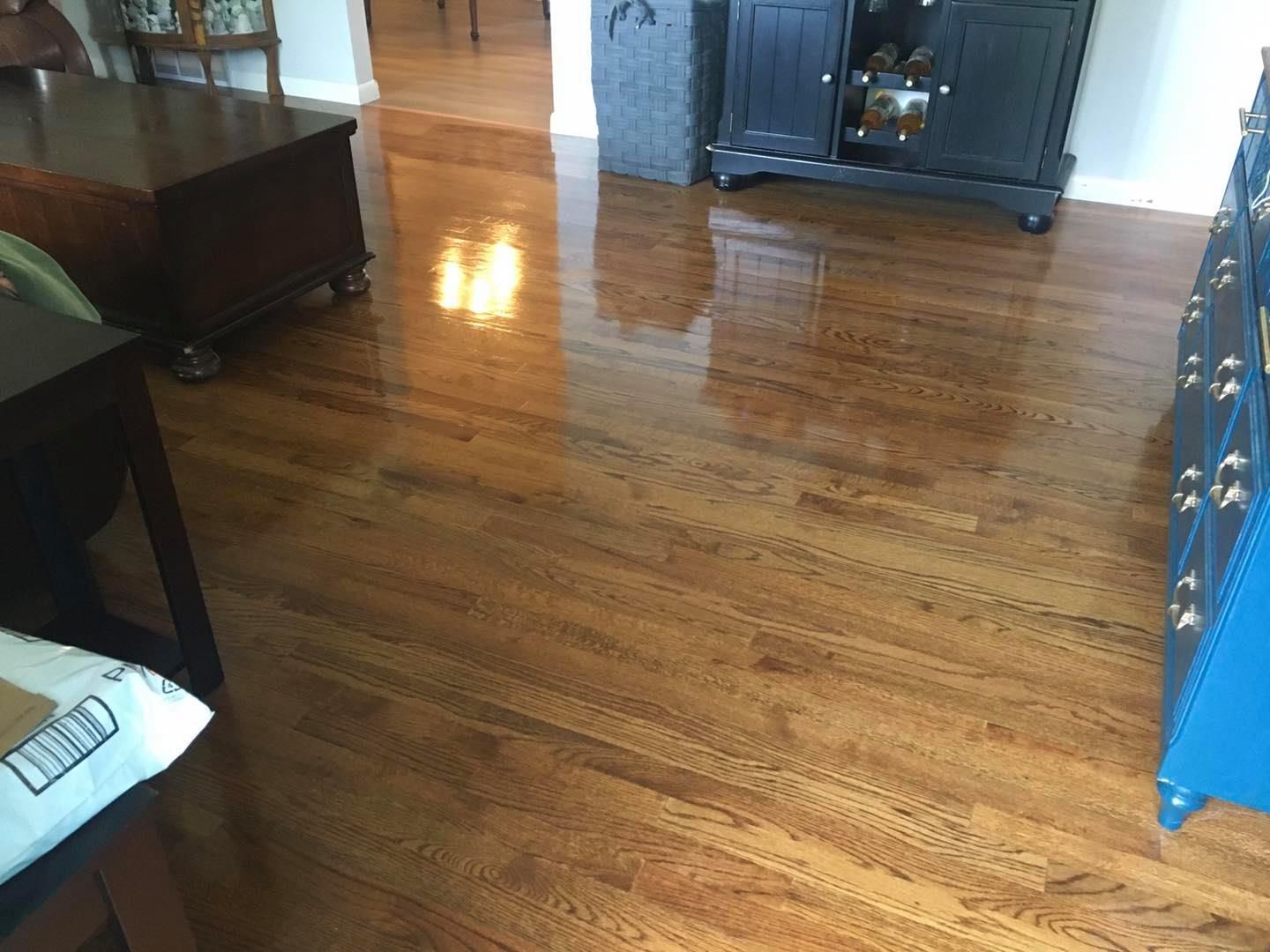 Polished wooden floor in a living room with furniture along the edges and sunlight reflecting on the floor