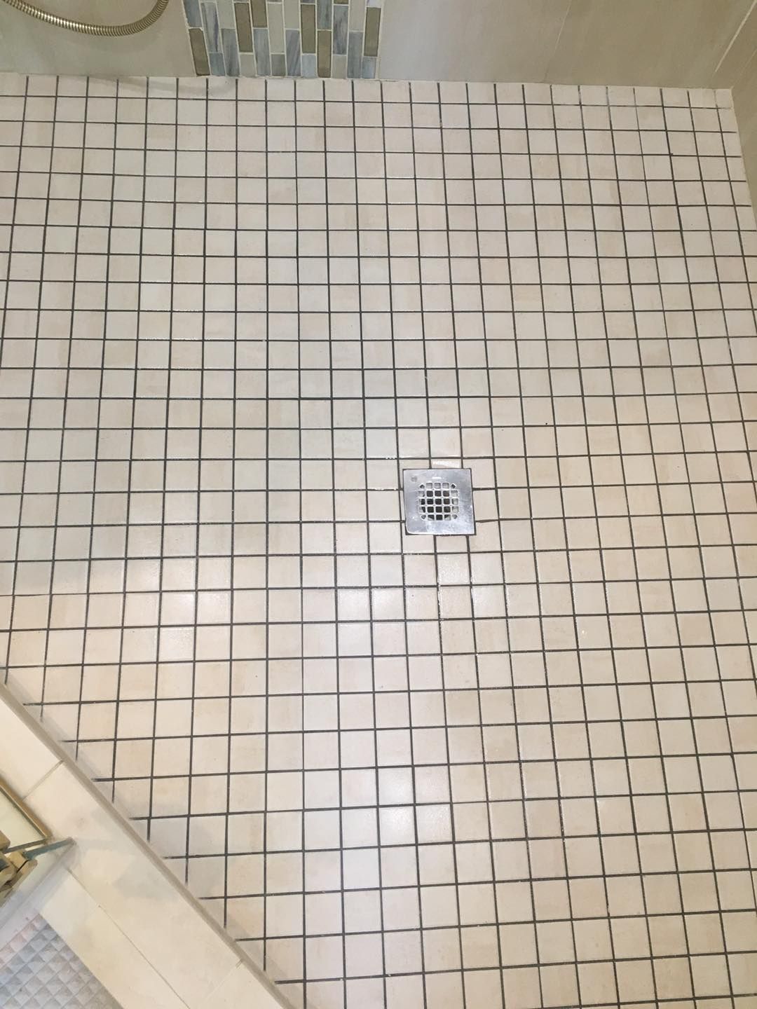 Tiled bathroom floor with a small square drain cover near the center