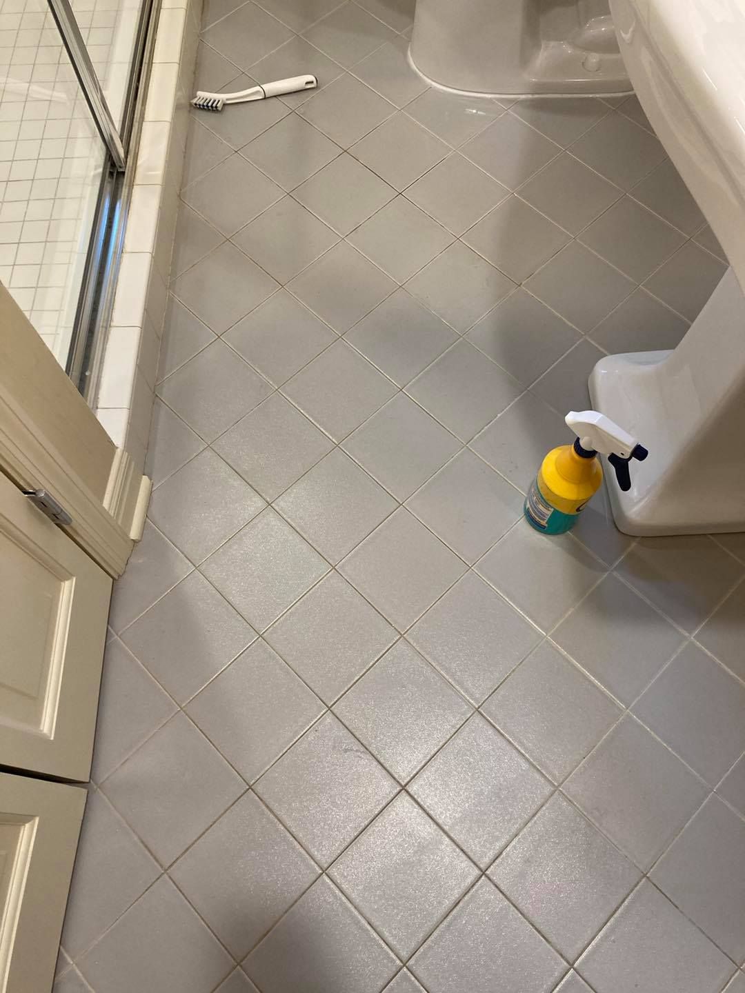 Bathroom floor with gray tile, white door, sink edge, and a spray cleaner bottle.