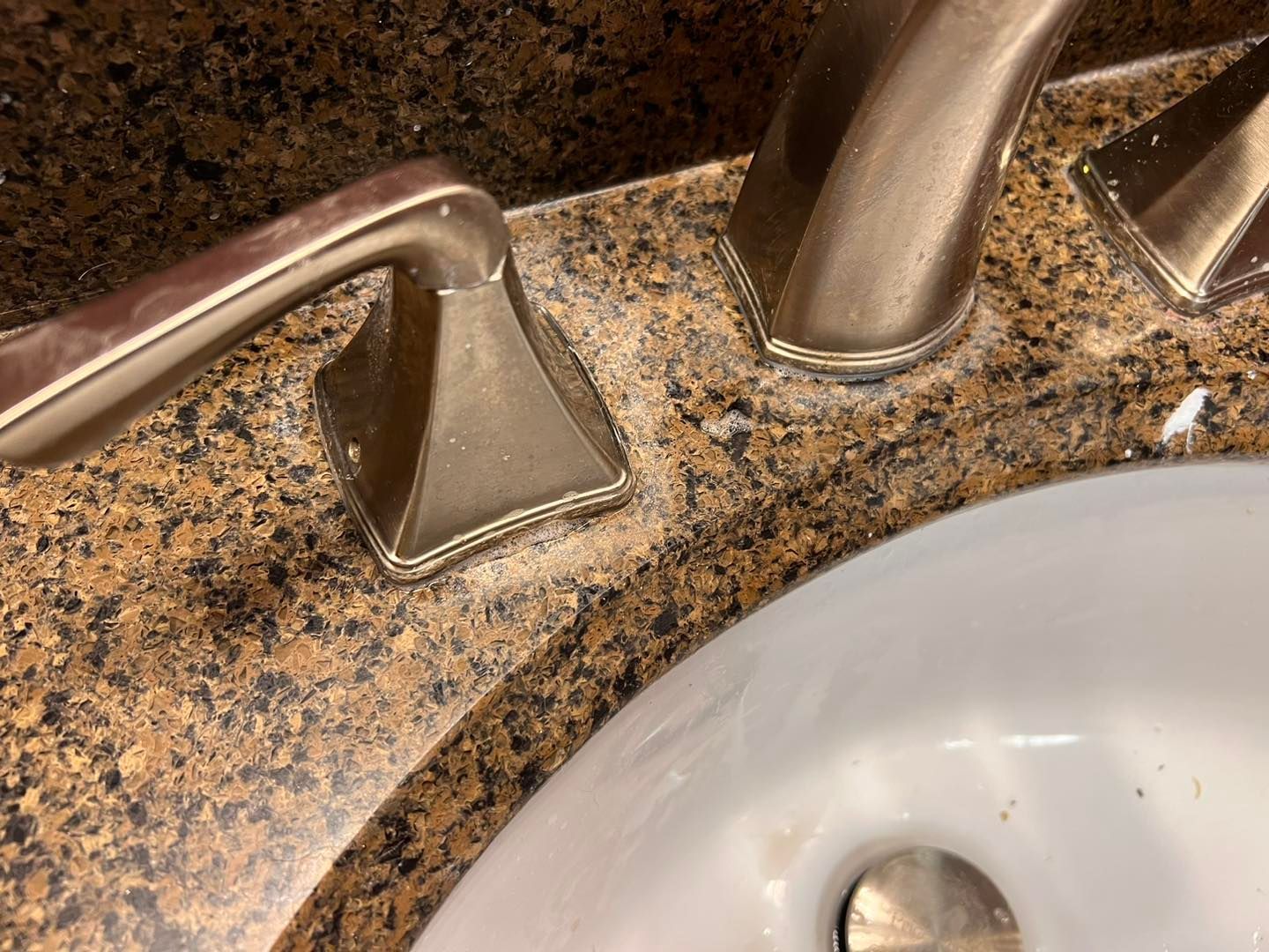 Bathroom sink faucet and handles on a speckled countertop, with part of the white sink visible.