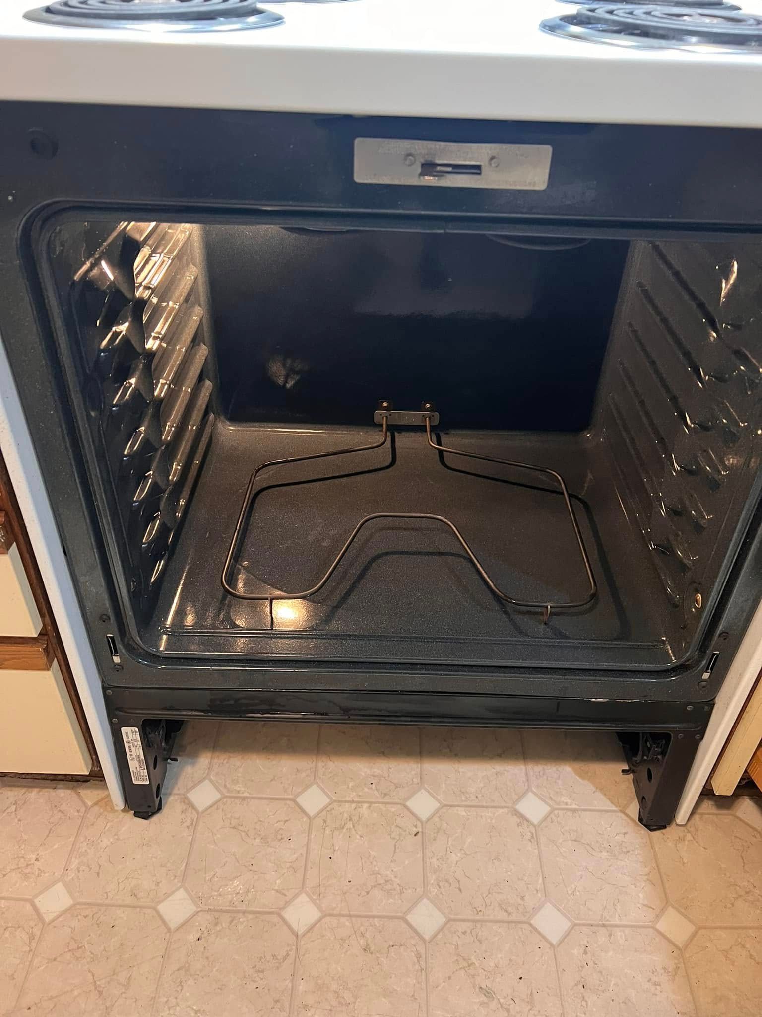 Open oven with a metal baking tray inside and a patterned linoleum floor below