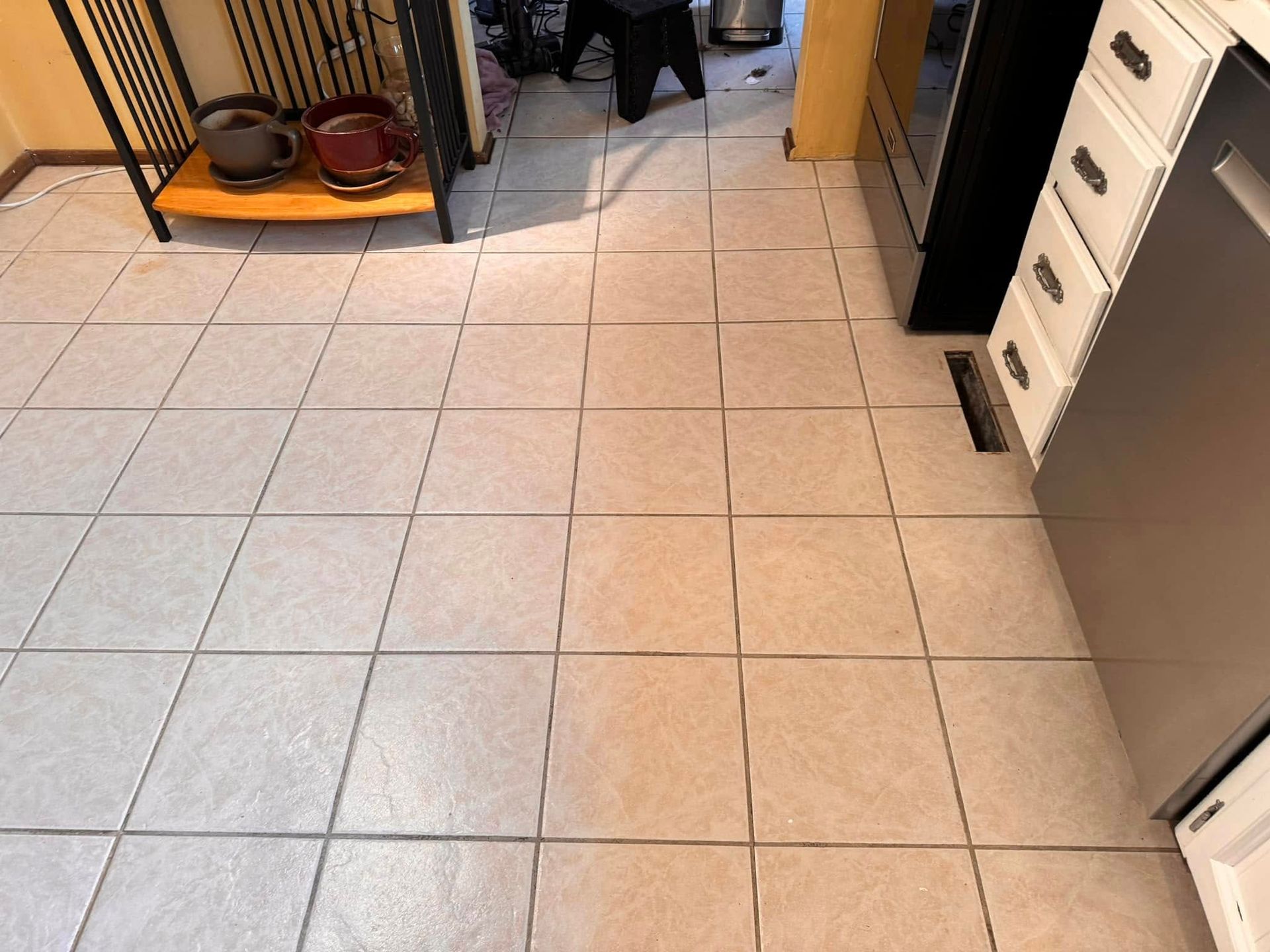Kitchen floor with light gray tiles, cabinets on the right, and pet bowls near a doorway.