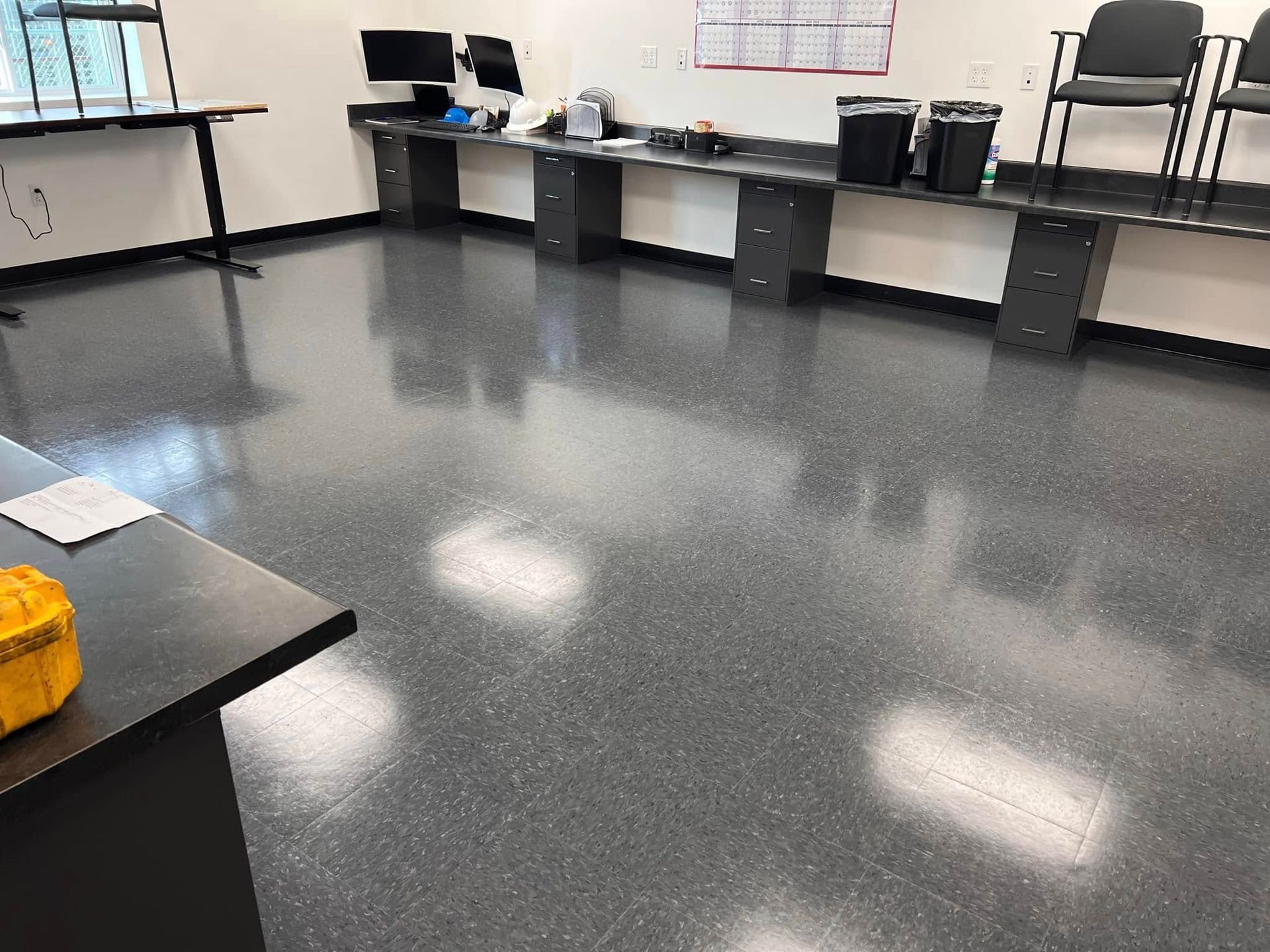 Empty classroom with desks, chairs, and a glossy gray floor reflecting ceiling lights