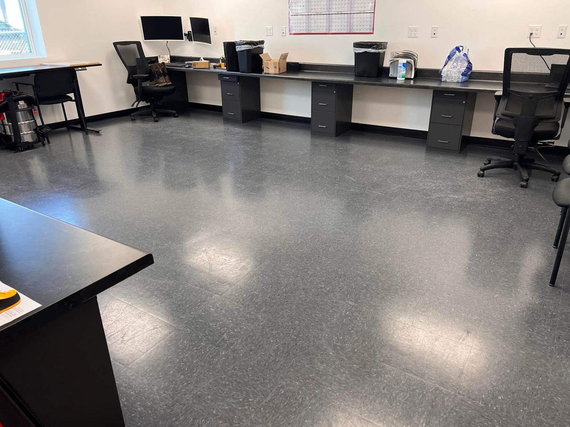 Office with desks, computer stations, black chairs, and a gray speckled floor.