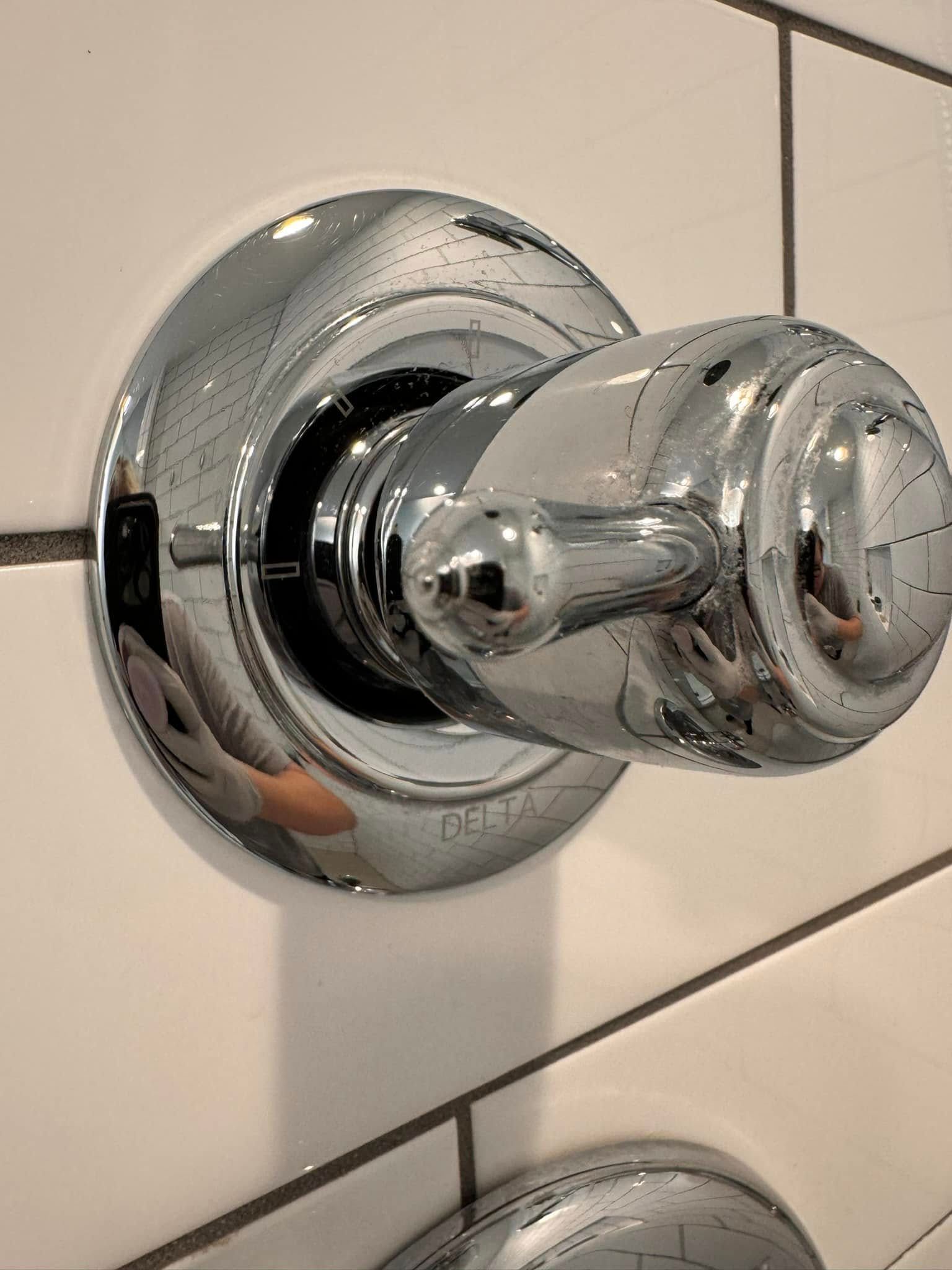 Chrome shower control knob on a tiled bathroom wall.