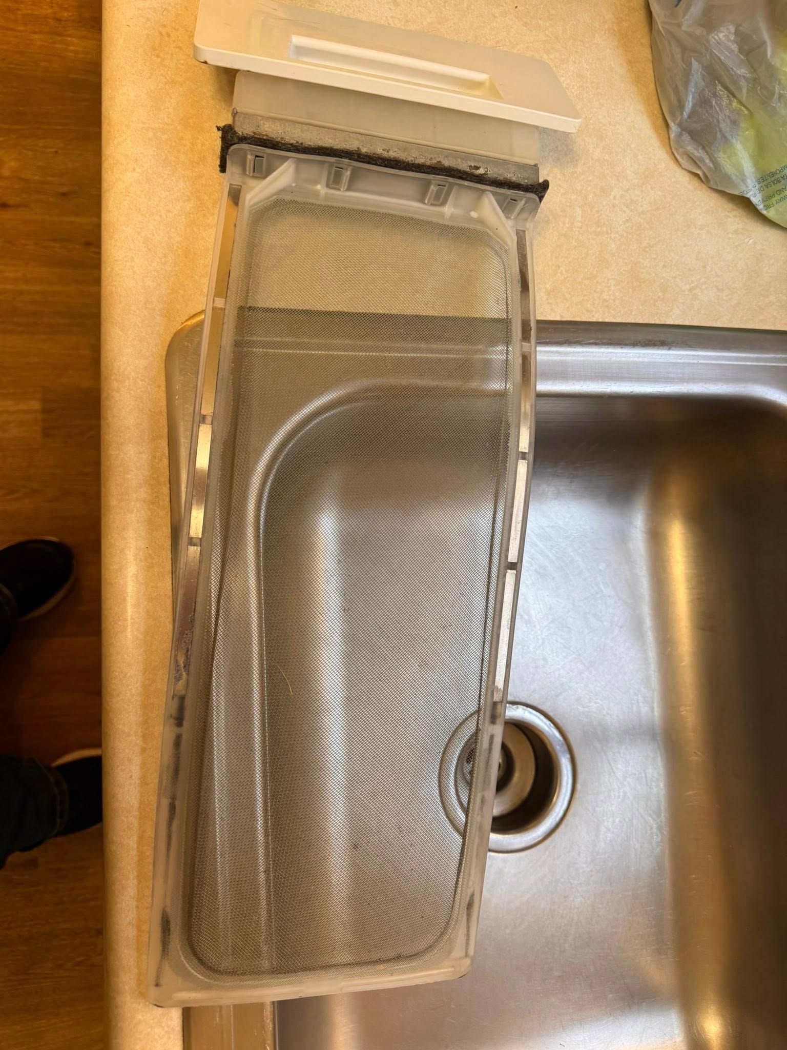 Metal mesh sink strainer resting across a stainless-steel kitchen sink drain on a beige countertop