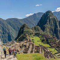 Tourists hiking above the stone terraces of Machu Picchu with green mountains in the background