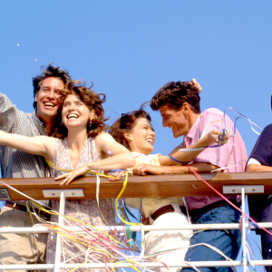 Four smiling people on a boat, surrounded by colorful streamers under a blue sky.