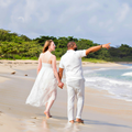 Couple walking barefoot on a sandy beach, holding hands, with one pointing toward the shoreline.