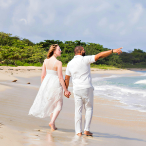 Couple walking barefoot on a sandy beach, holding hands, with one pointing toward the shoreline.